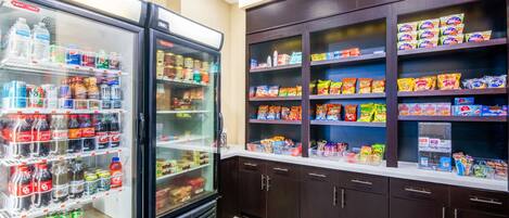 A snack and beverage refrigerator stocked with various drinks and snacks, and a shelf unit with packaged snacks.