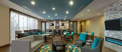 A hotel lobby with a sofa, chairs, a coffee table, a bar area, and a TV screen.