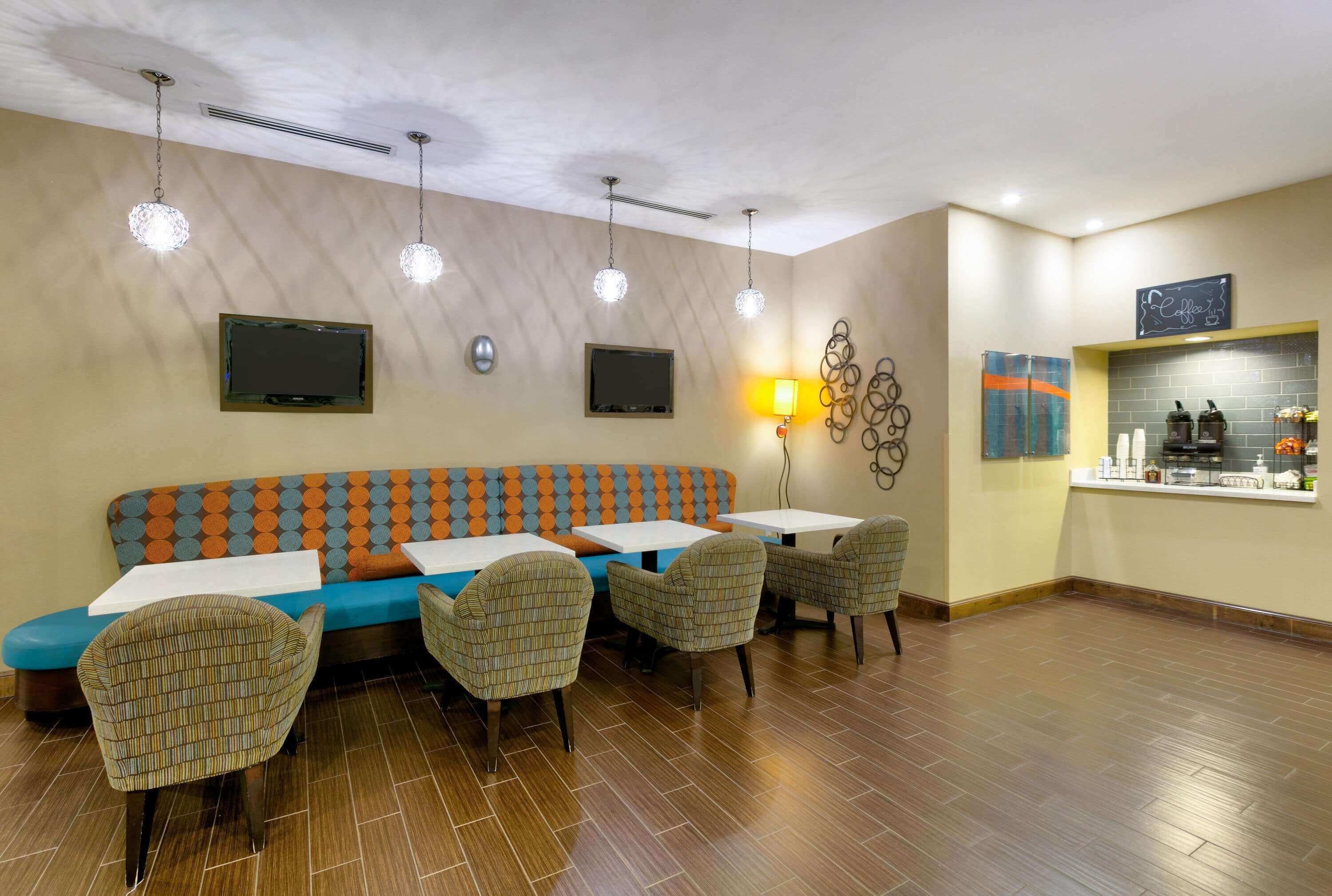 A restaurant with a blue and orange patterned sofa, four chairs, two tables, and a bar area with a coffee sign.