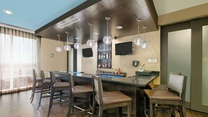 Un espace bar doté d’un long comptoir, de nombreux tabourets et de lustres en cristal suspendus.