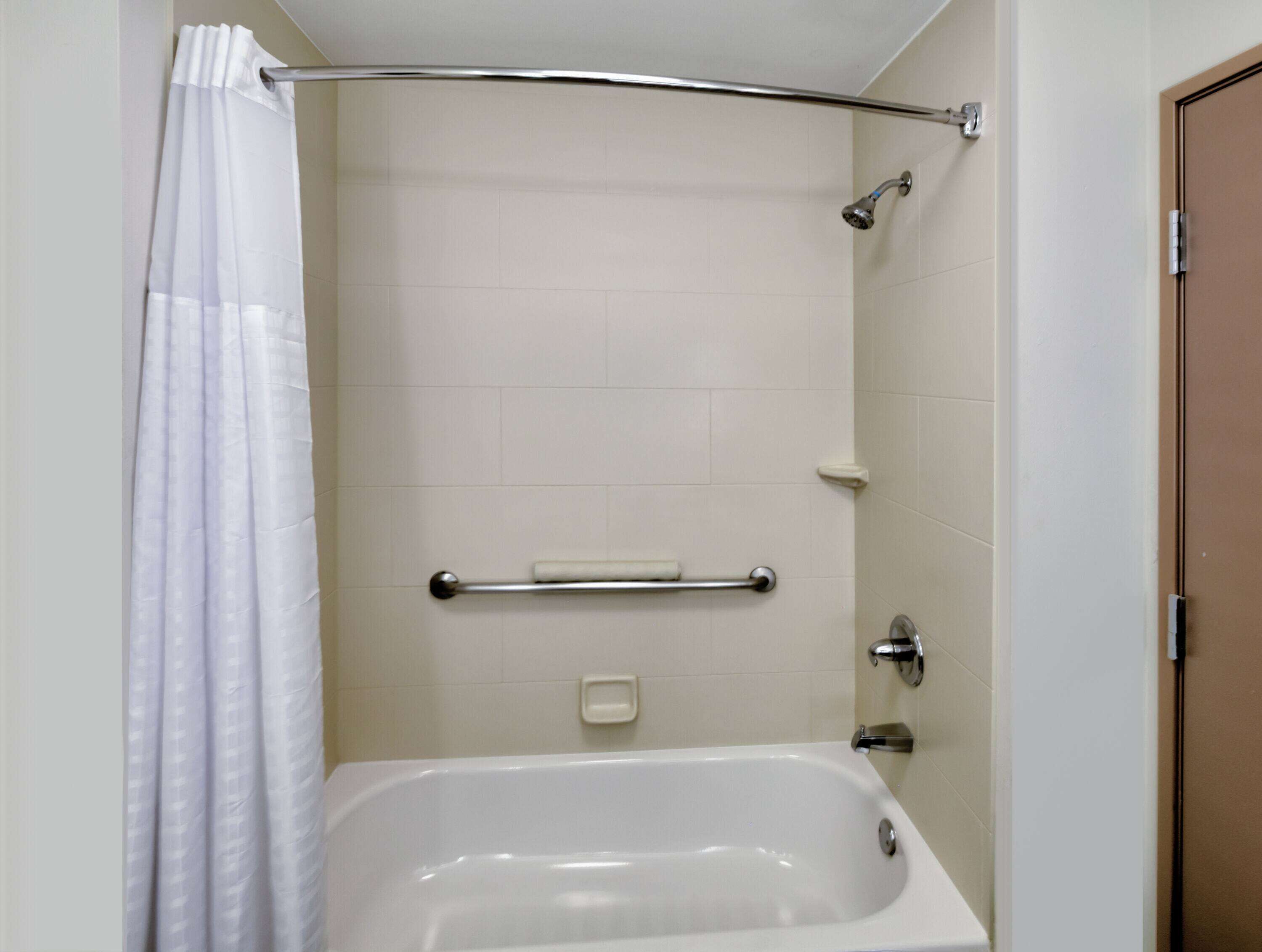 Un baño con bañera, cortina de ducha, barra de apoyo y puerta.