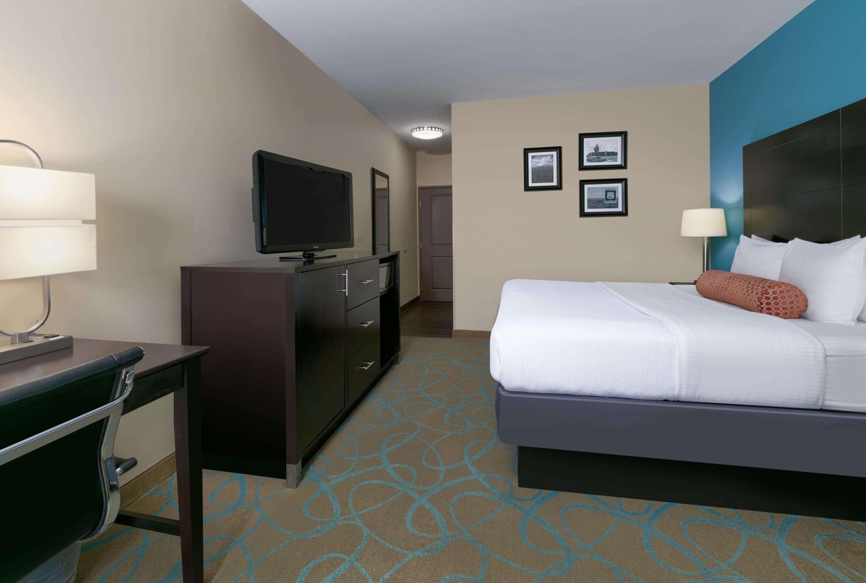 A hotel room with a bed, a desk with a lamp, a television, and a dresser.