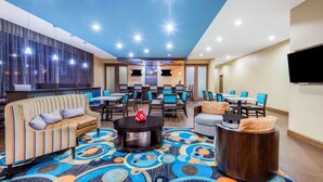 Un hall d’hôtel avec des canapés à rayures, une moquette à motifs et un téléviseur fixé au mur.