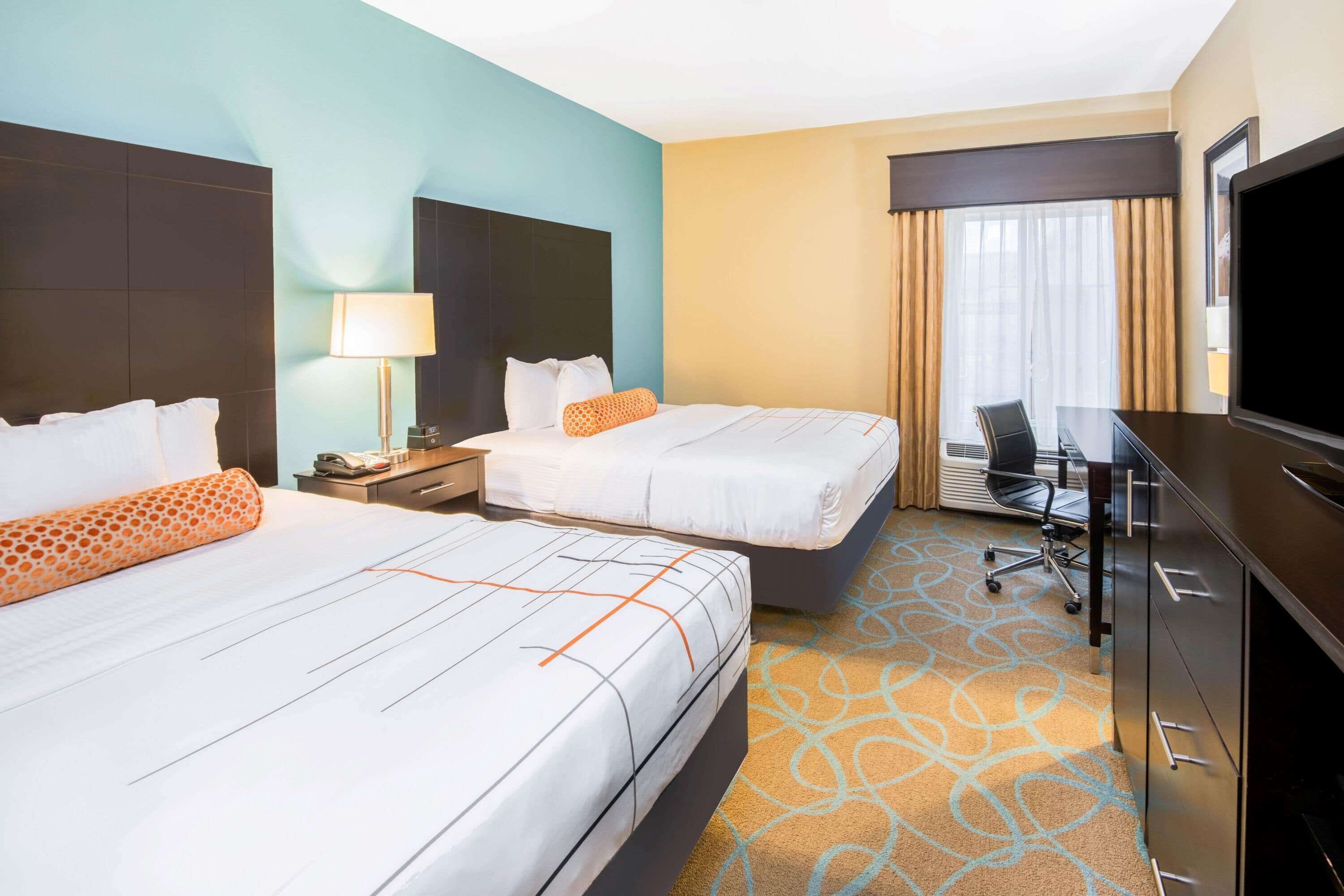 A hotel room with two beds, a desk, a chair, a TV, and a window with curtains.