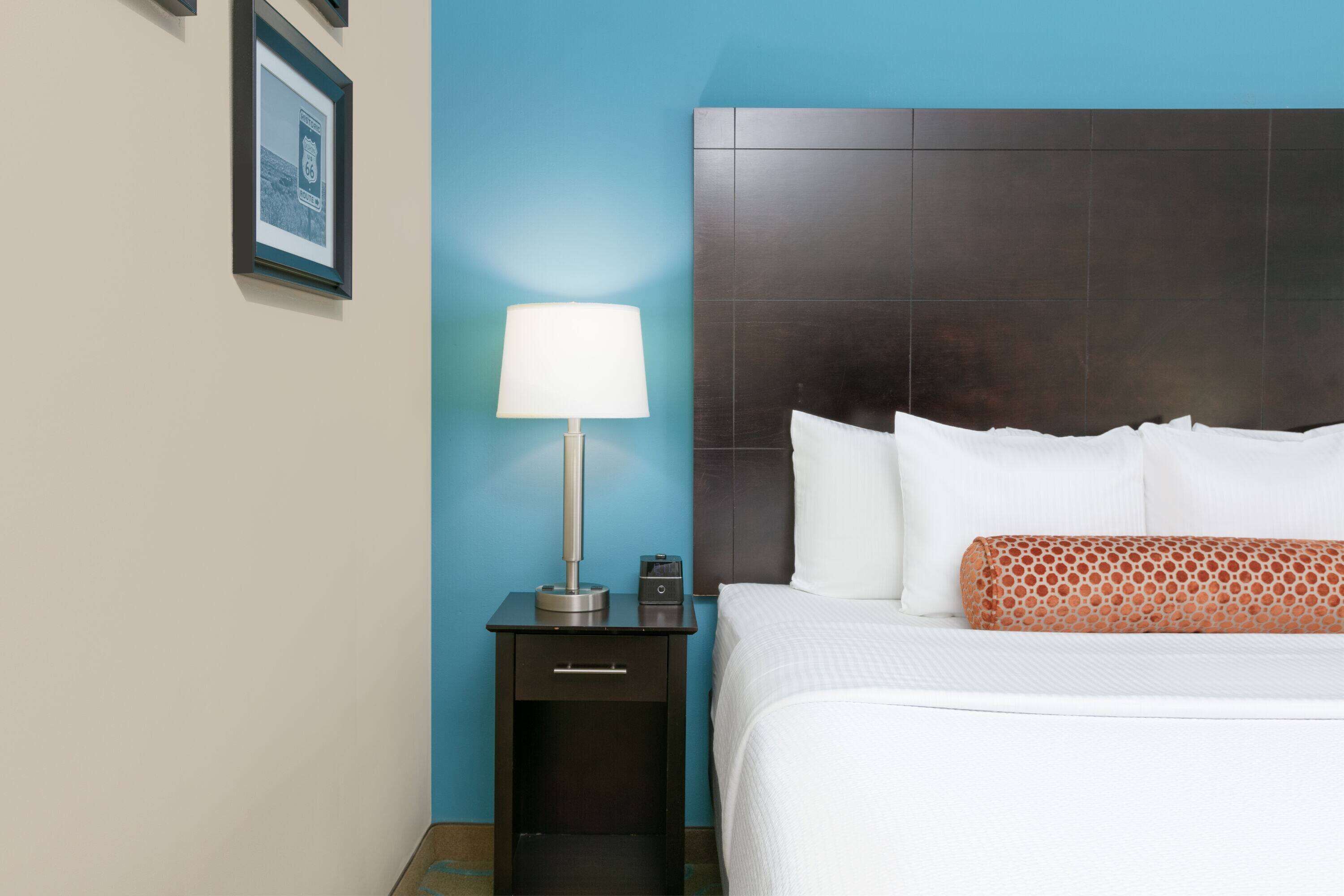 A hotel room with a bed, a nightstand, a lamp, and a framed picture on the wall.