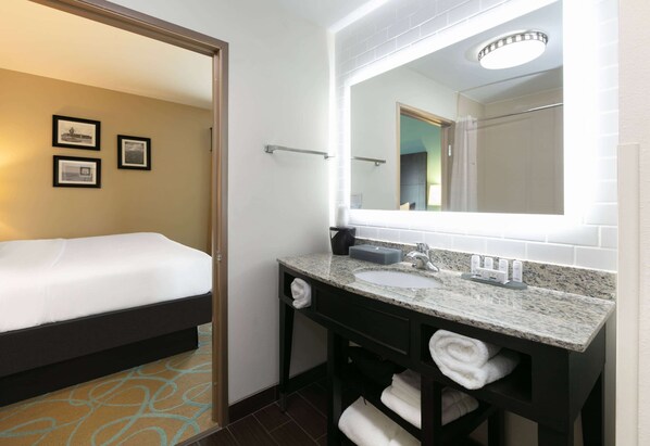 A hotel room with a bed, a bathroom with a sink and mirror, and a towel rack. - La Quinta Inn & Suites by Wyndham Clinton Historic Route 66 (Clinton)