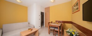 A compact living space with a sofa, a dining table with chairs, a wooden cabinet, and a TV mounted on the wall. - Apartments Katoro Plava Laguna (Umag)