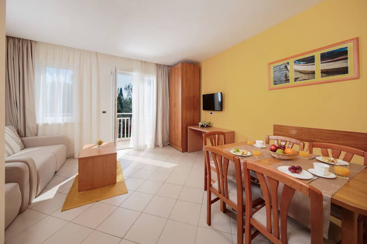 Ett modernt hotellrum med en soffa, ett matbord, en frukostplats och en tv på väggen.