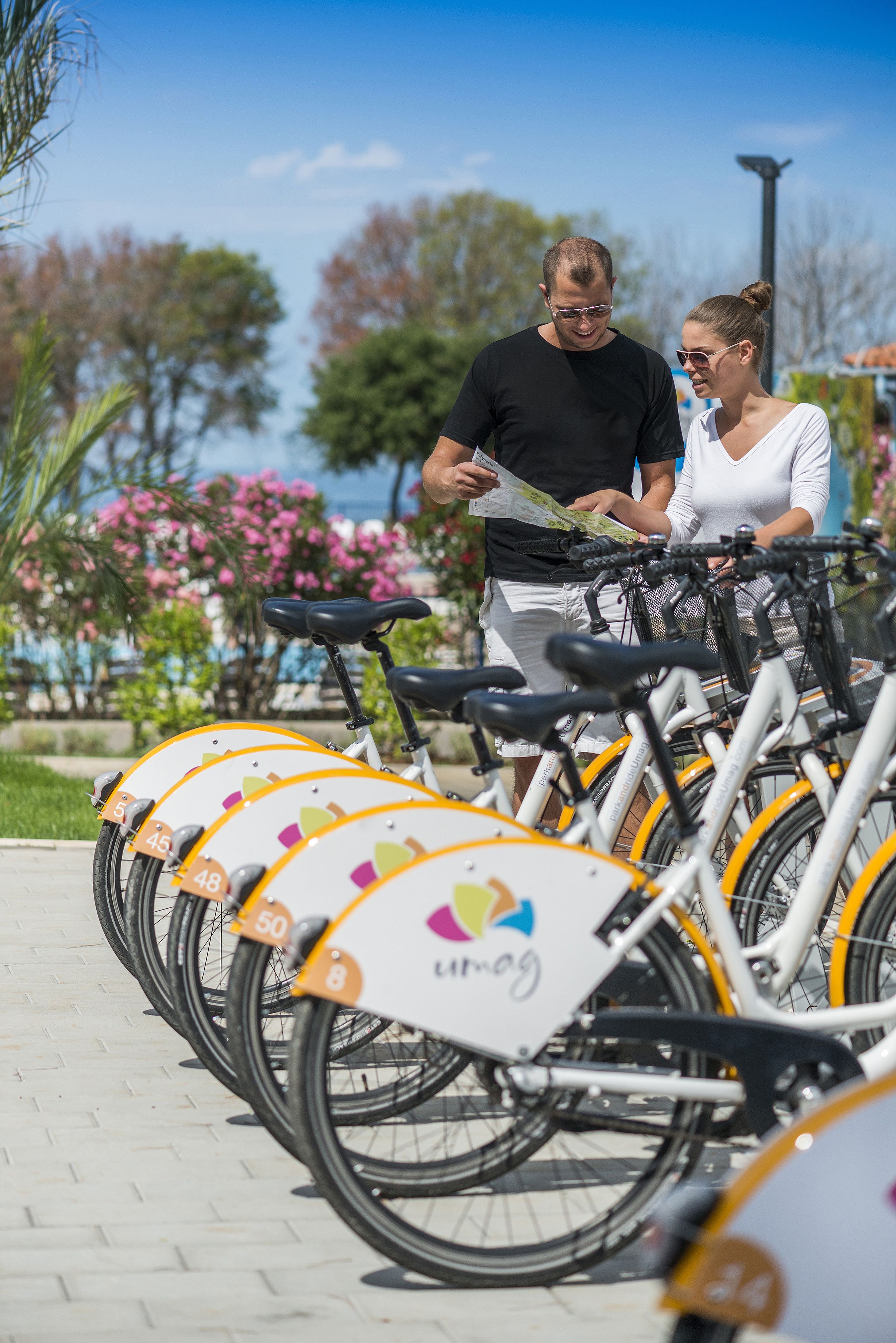 A row of bicycles with numbers on the front, a person holding a map, and a woman standing beside them.