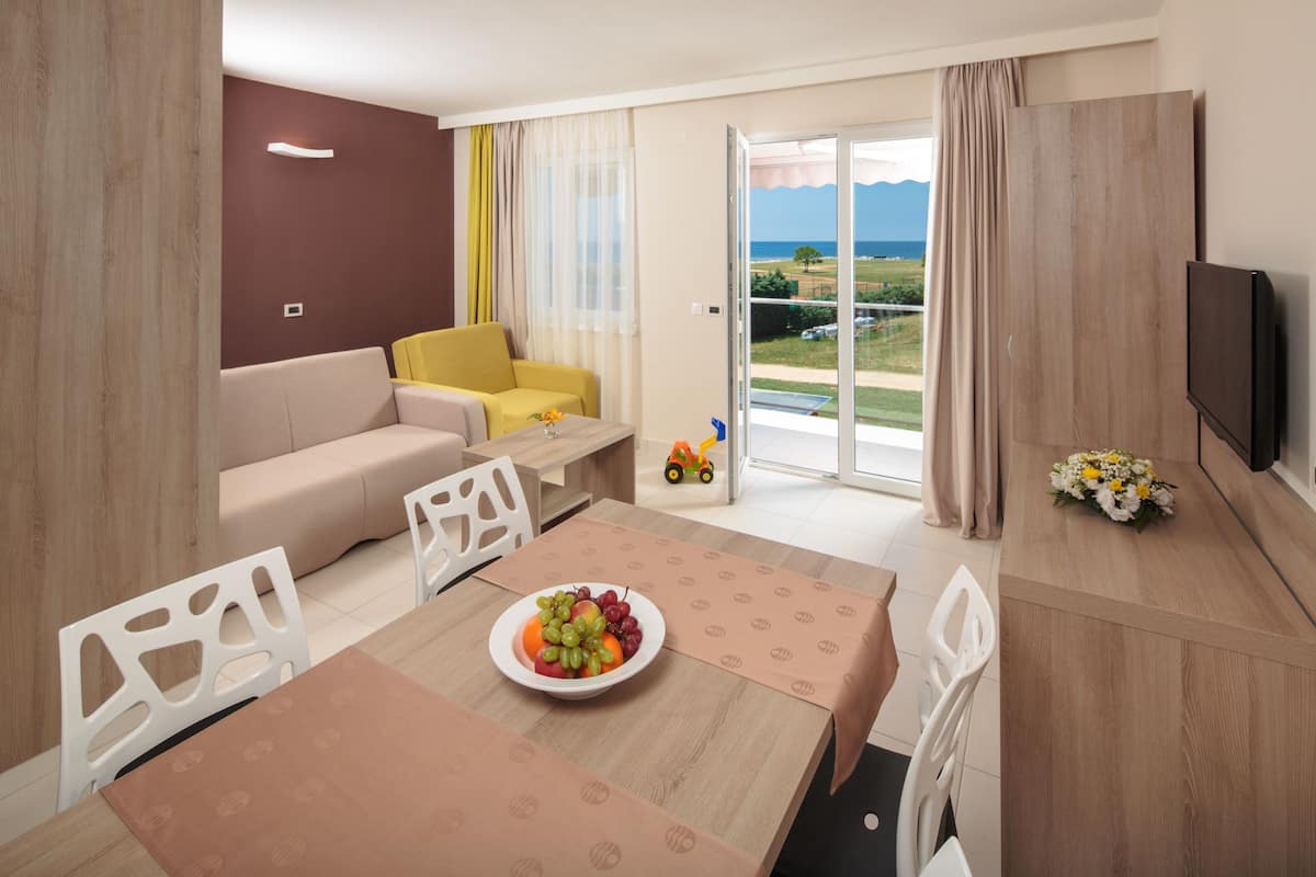 Ett modernt hotellrum med en matplats, en soffa, en TV och en balkong med utsikt över havet.