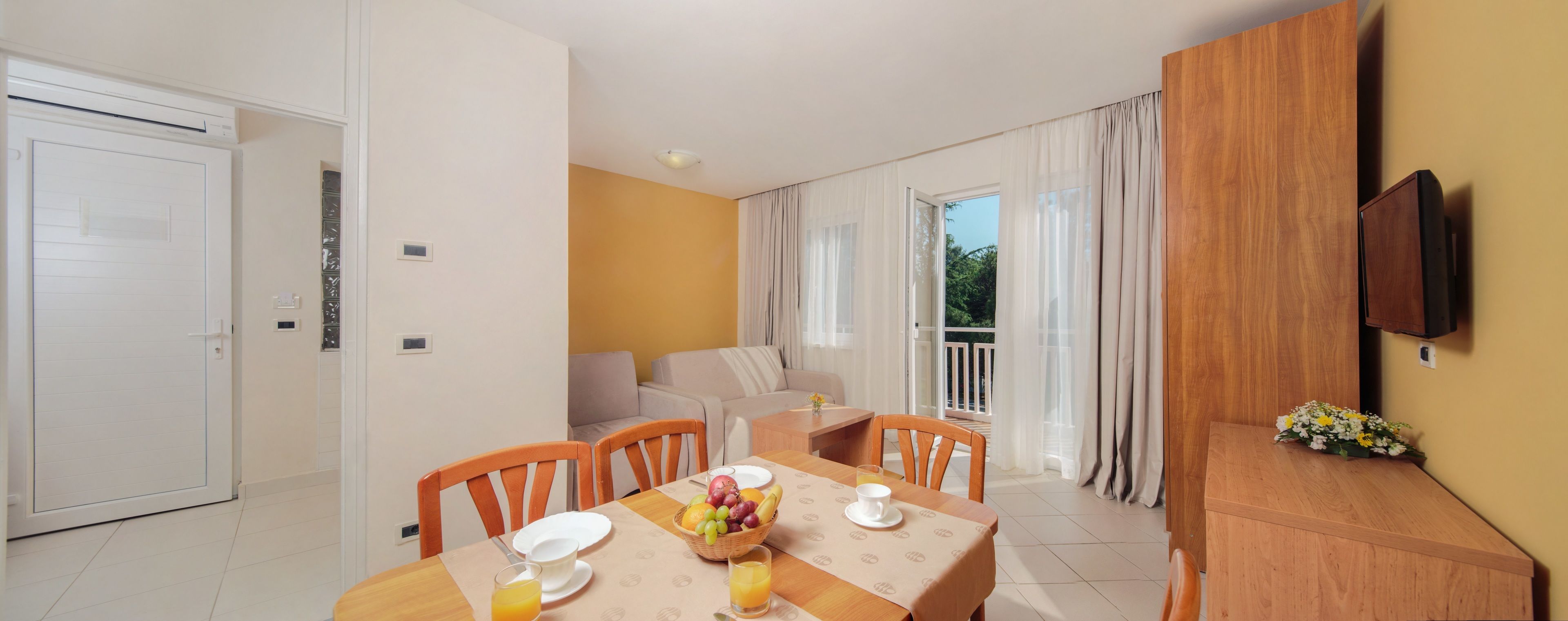 A dining area with a table set for two, a sofa, and a balcony with curtains.