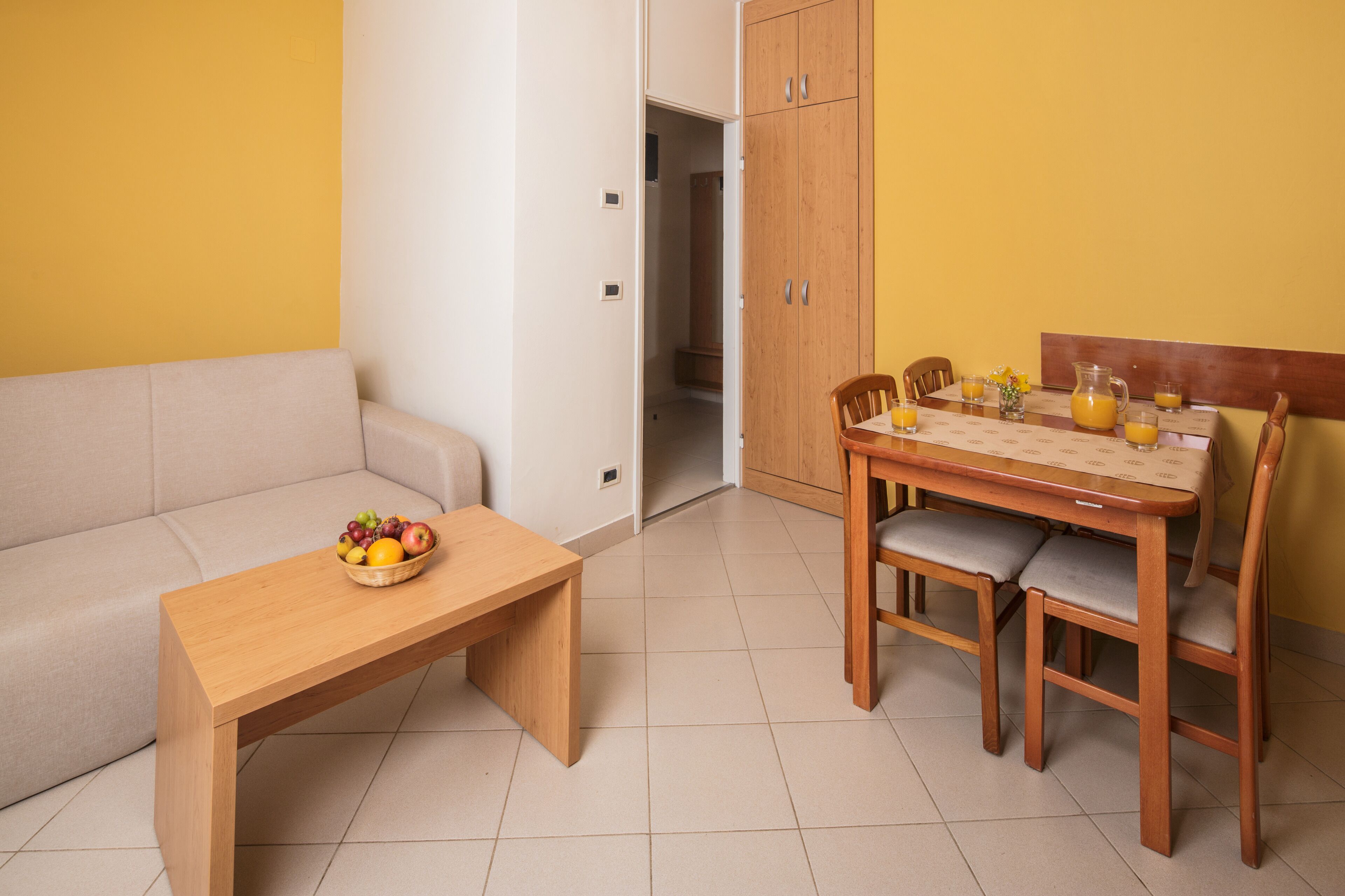 Ein kleiner, heller Raum mit einem Esstisch gedeckt für das Frühstück, einer Couch und einem Holzkasten.