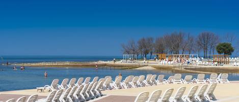 A beachside pool area with rows of white lounge chairs and a clear view of the sea.