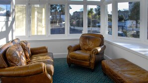 A room with a leather sofa, armchair, and ottoman, large windows with a view of the street, and a patterned carpet. - New Westcliff Hotel (Bournemouth)