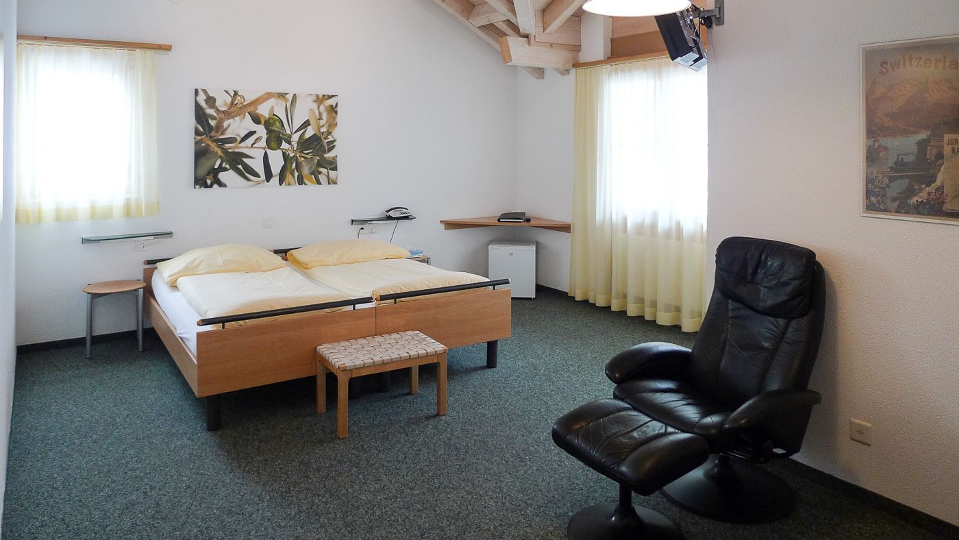 A hotel room with a bed, a chair, a small table, and a desk.