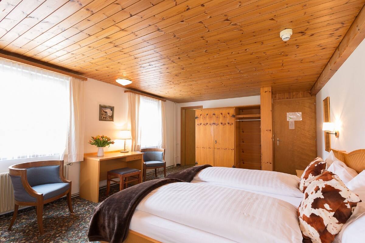 Une chambre d’hôtel avec un plafond en bois, un lit avec un oreiller à motifs marron et blanc, un bureau avec une chaise et une armoire.