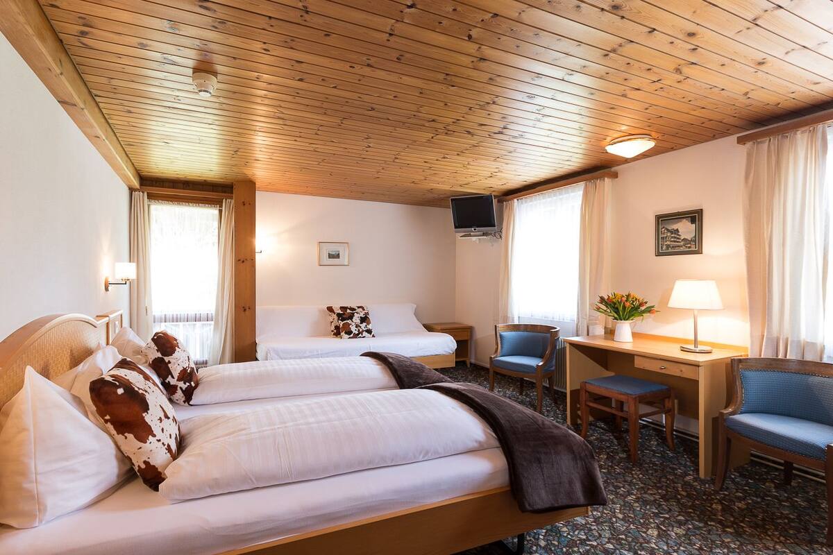 Une chambre d’hôtel avec deux lits, un bureau, une chaise, une télévision et une fenêtre avec des rideaux.