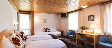 A hotel room with two beds, a desk, a chair, a TV, and a window with curtains.