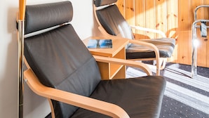 Een kamer met twee zwarte leren fauteuils, een houten vloer, een houten wandpaneel en een vloerlamp.