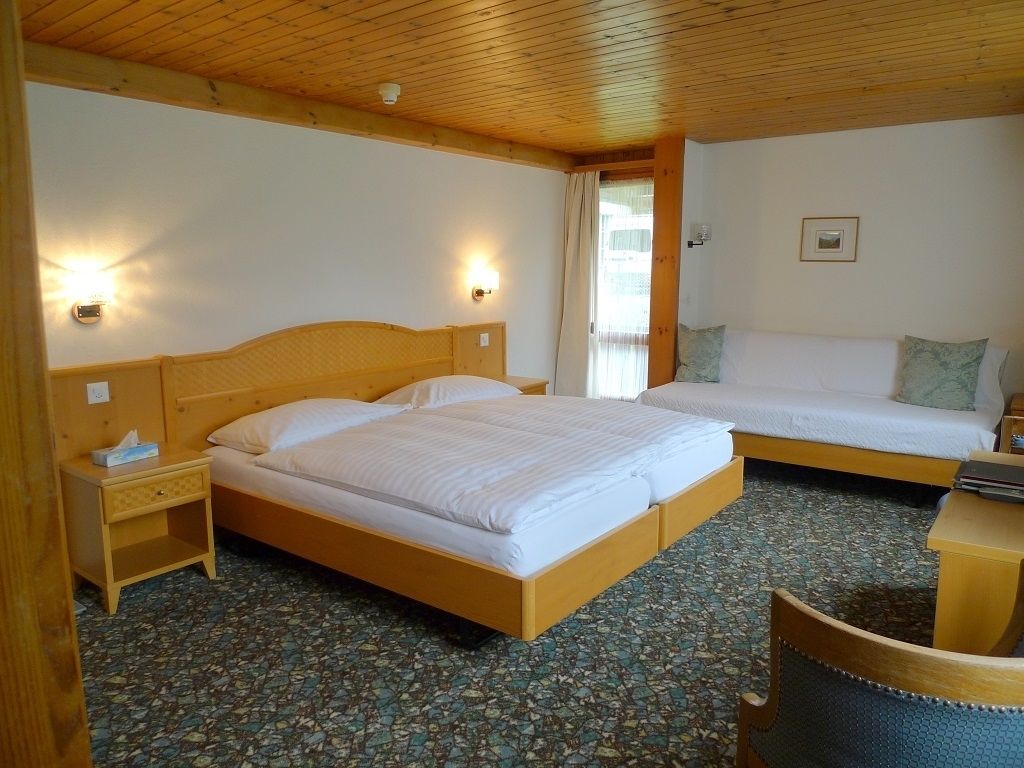 A hotel room with a wooden ceiling, a large bed with a wooden headboard, a smaller bed, a nightstand with a lamp, and a chair.