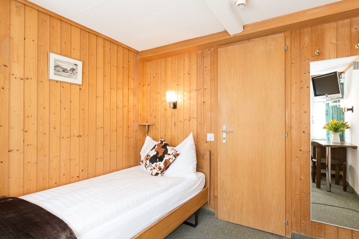 Una habitación con paneles de madera, una cama, una mesita de noche, una lámpara y un espejo.