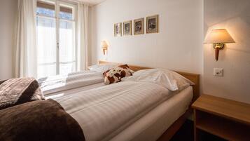 Ein Hotelzimmer mit zwei Betten, einem hölzernen Kopfteil, einem Nachttisch, einer Lampe und einem Fenster mit Vorhängen.