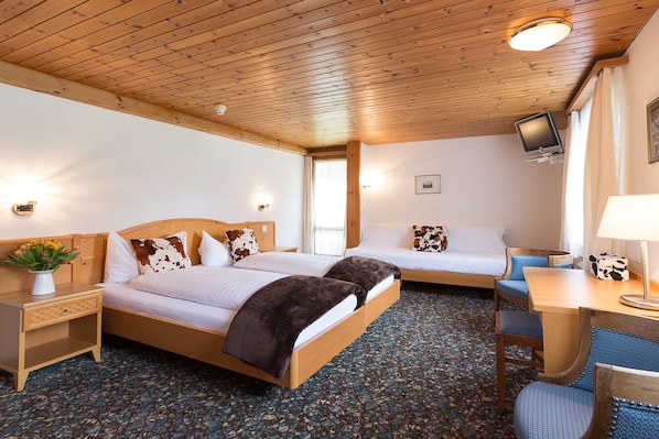 Habitación de hotel con techo de madera, dos camas con ropa de cama marrón y blanca, un escritorio con lámpara y televisión en la pared.