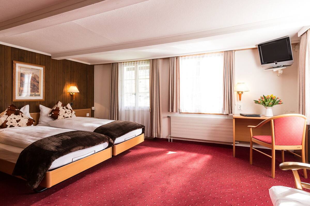 Une chambre d’hôtel avec un lit, un bureau, une chaise, une télévision et une fenêtre avec des rideaux.