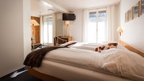 Een hotelkamer met twee bedden, een bureau, een stoel, een aan de muur bevestigde televisie en een raam met gordijnen.
