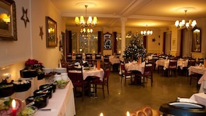 Een eetruimte met meerdere tafels gedekt voor een maaltijd, een kerstboom en diverse etenswaren gepresenteerd op een buffet.