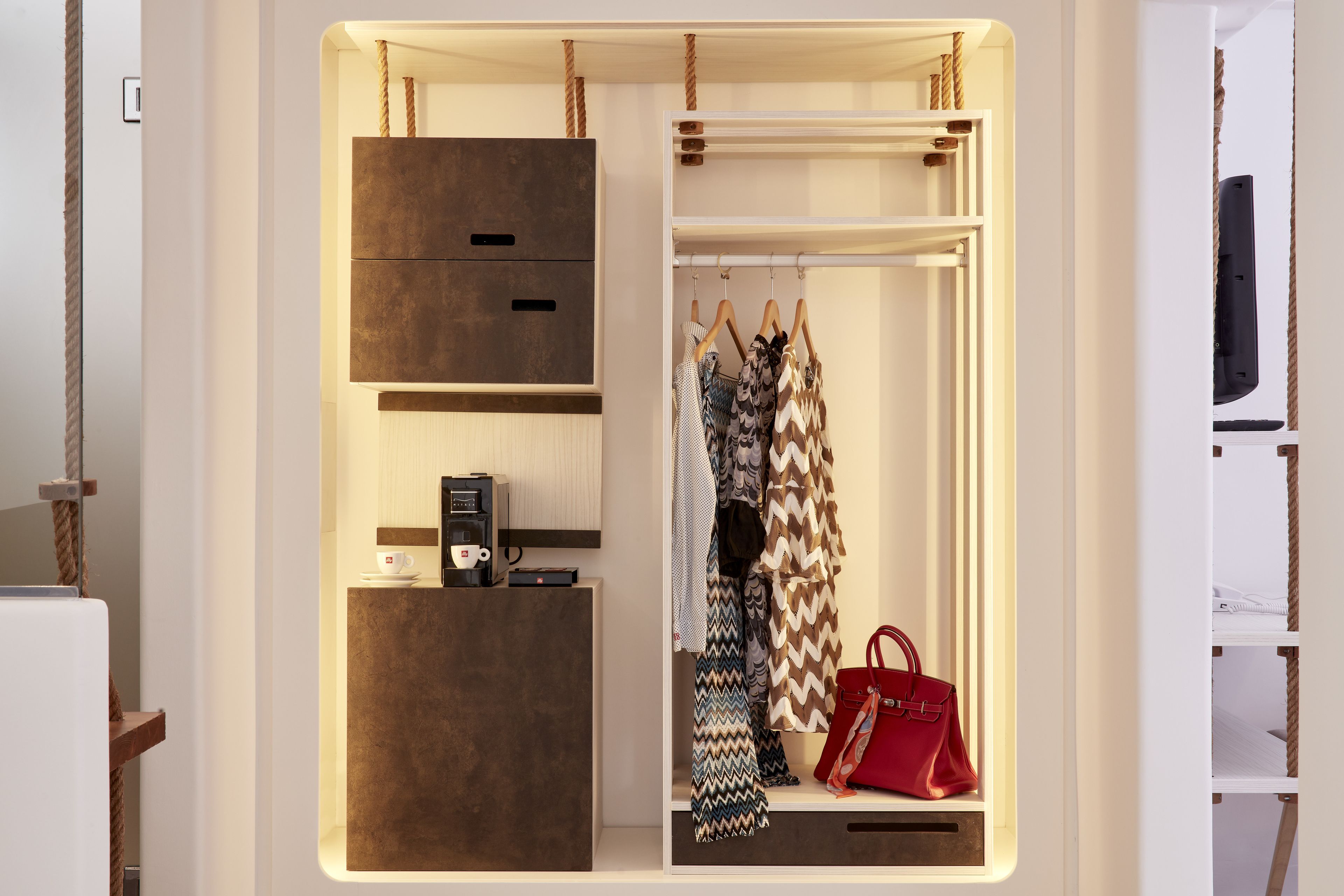 Un vestidor amplio con espacio para colgar ropa y cajones, una cafetera y un bolso rojo.