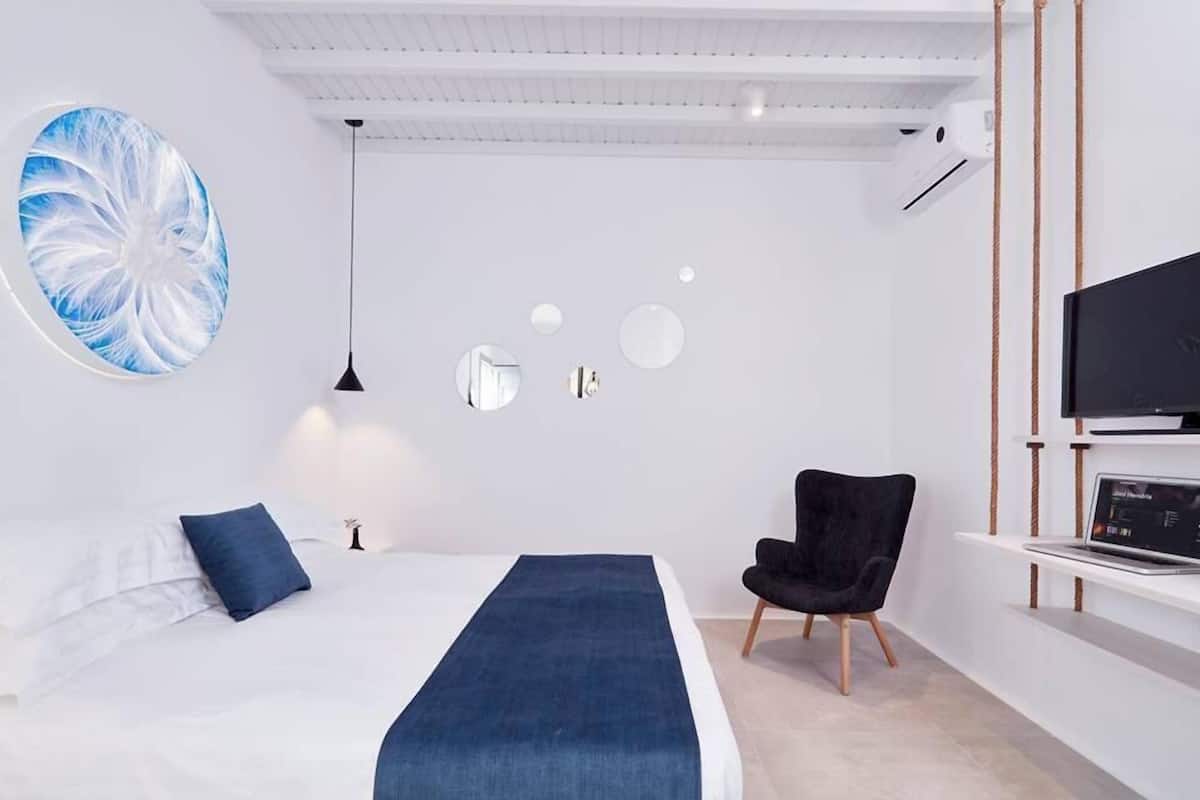 Une chambre moderne avec un lit, une chaise noire, un téléviseur et une œuvre d’art murale.