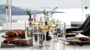 A table set with wine glasses, plates of food, and a view of the sea. - Absolute Mykonos Suites & More (Mykonos)
