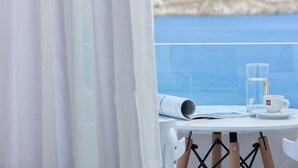 A table with a clear glass, a rolled-up blueprint, and a white cup with a logo, overlooking a coastal view. - Absolute Mykonos Suites & More (Mykonos)