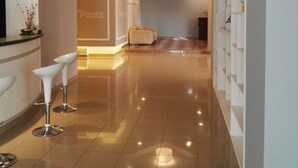 Zona de recepción de un hotel con diseño moderno, que incluye un mostrador de recepción, tres taburetes blancos y un área de estar con sofá.