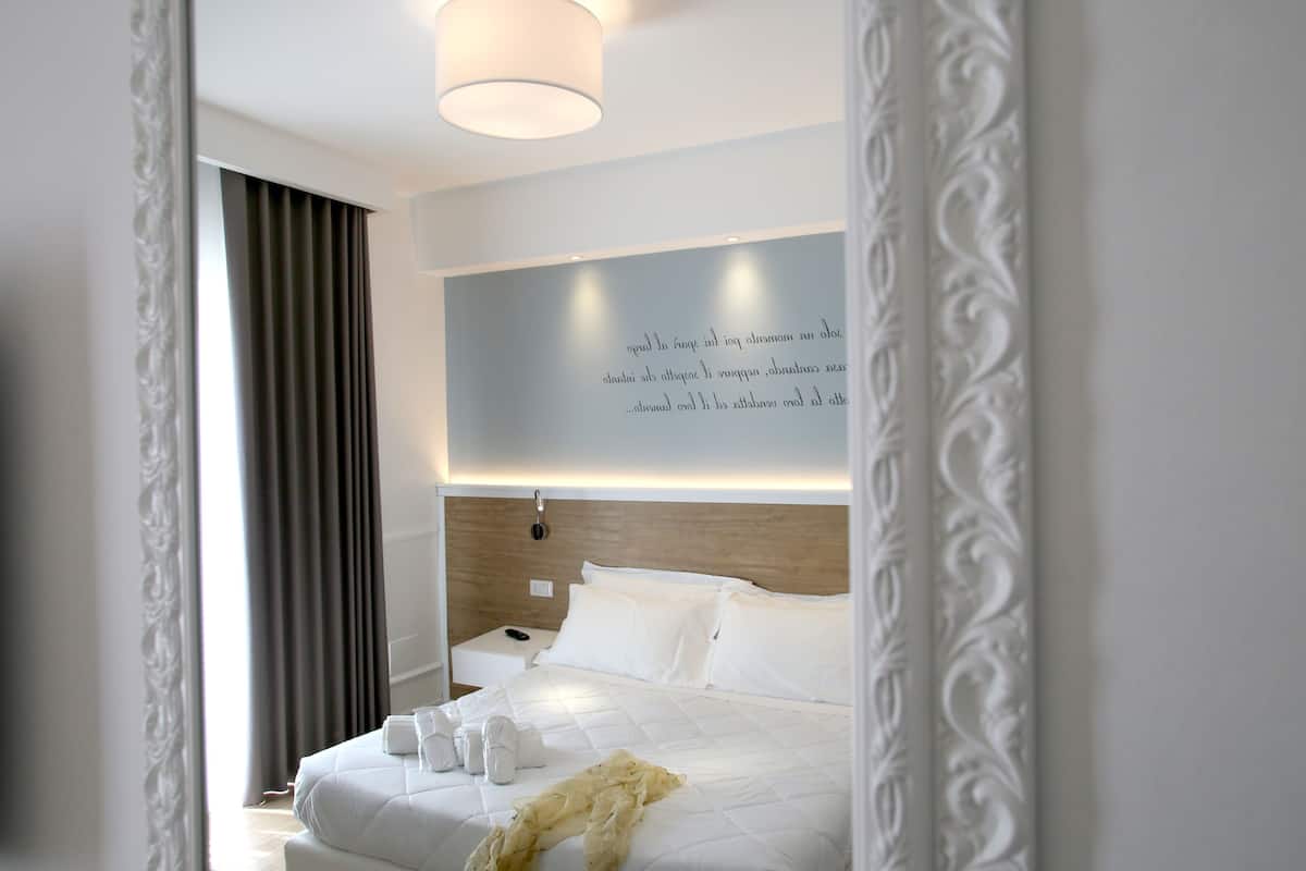A modern hotel room with a neatly made bed, a bedside table with a lamp, and a large window with curtains.