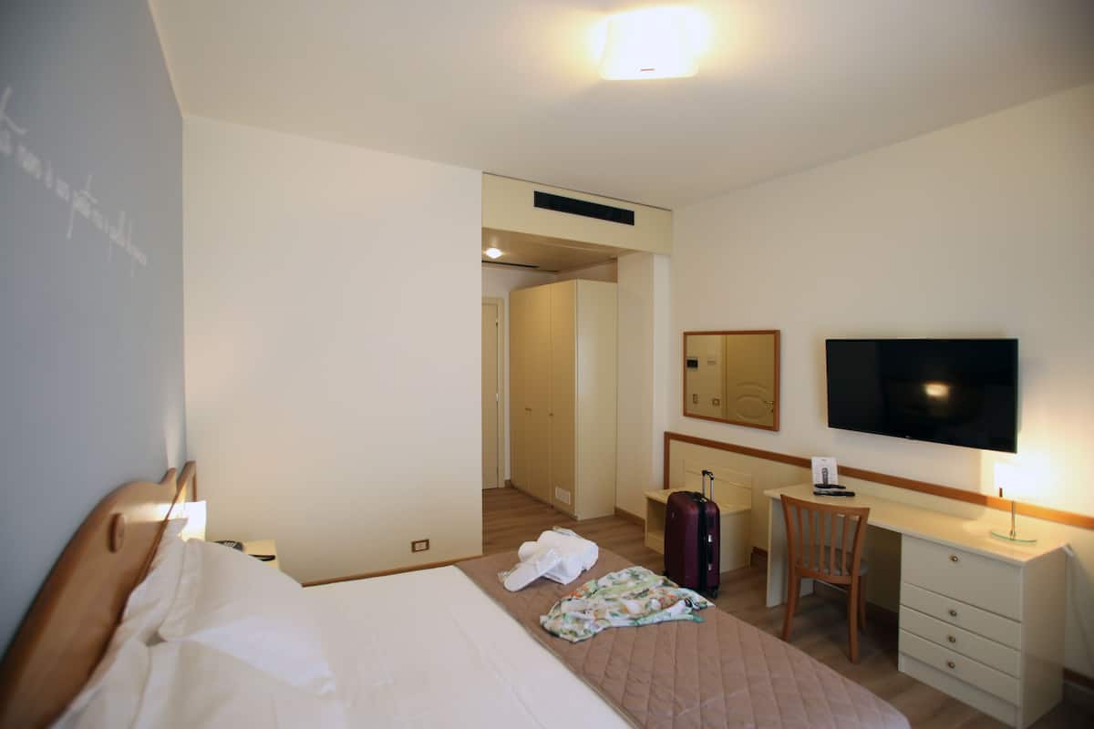 A hotel room with a bed, a desk, a chair, a TV, and a suitcase.