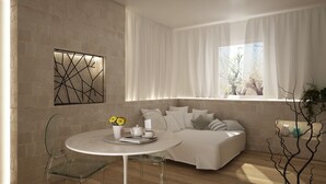 Una sala moderna con una mesa redonda blanca, un sofá con varios cojines, un adorno en la pared y una ventana con cortinas.