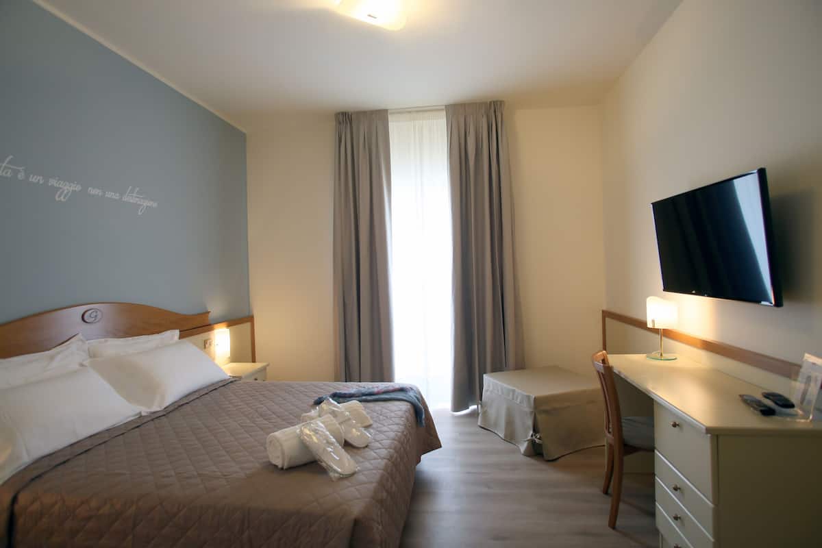 A hotel room with a bed, a desk, a chair, a TV, and a window with curtains.