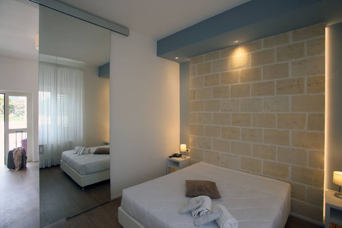 A modern hotel room with a large bed, a bedside table, and a brick accent wall.