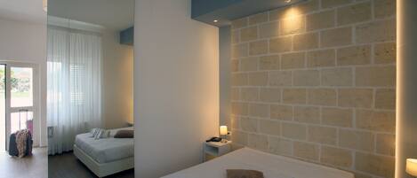 A modern hotel room with a large bed, a bedside table, and a brick accent wall.