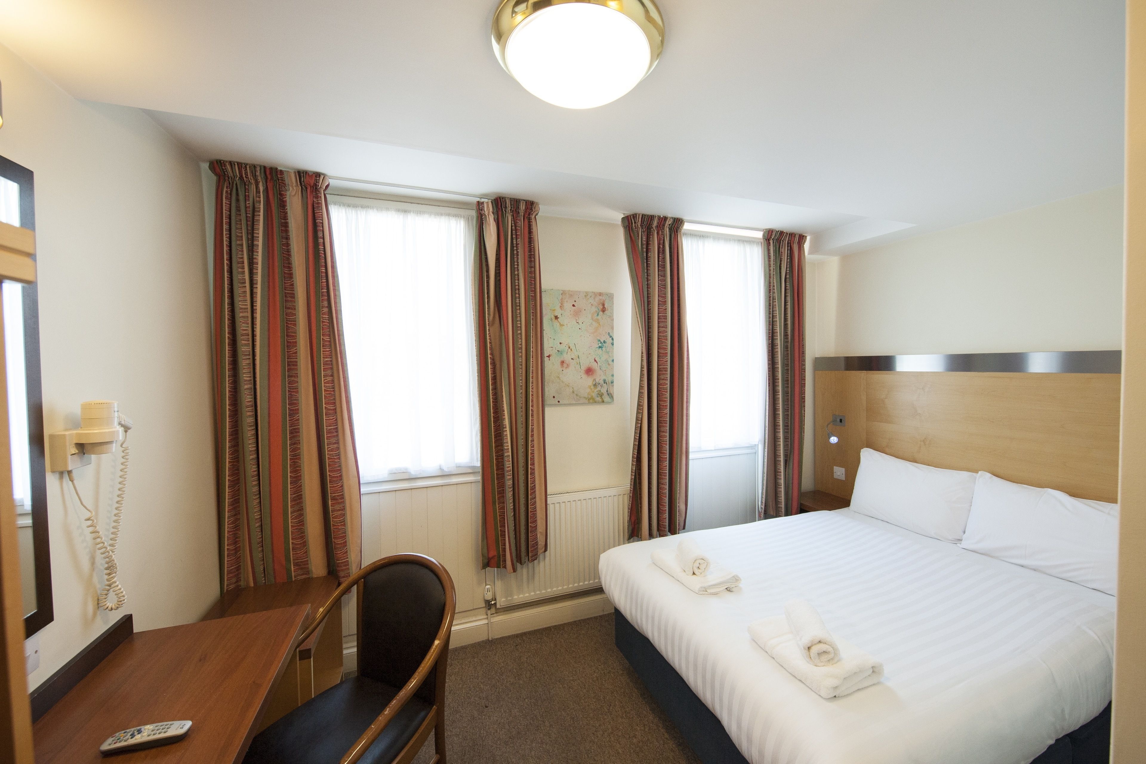 A hotel room with a bed, a desk with a chair, a telephone, and curtains.