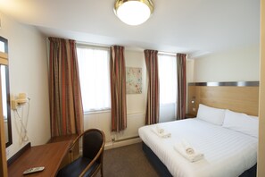 Een hotelkamer met een bed, een bureau met stoel, een telefoon en gordijnen.