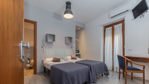 Habitación de hotel con dos camas, un escritorio, una silla, ducha y televisión.
