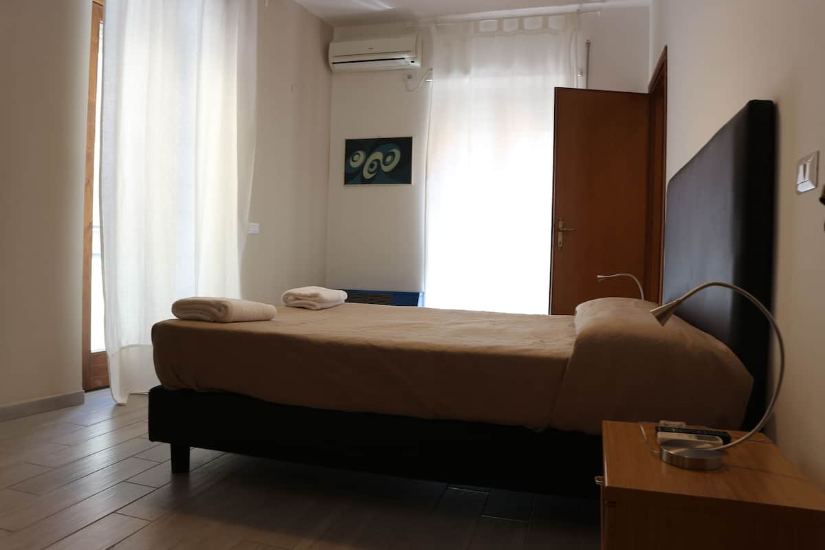 A bedroom with a bed, a bedside table, a wall-mounted air conditioner, and a door.