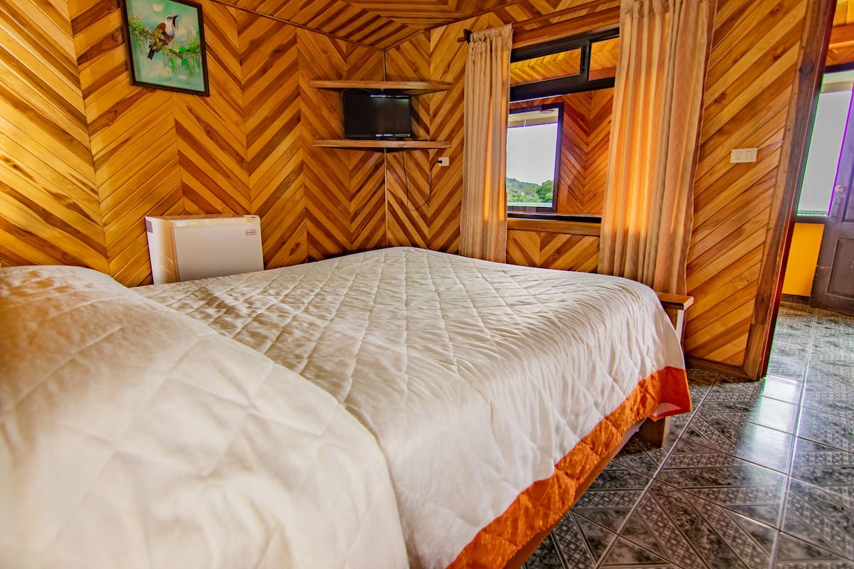 Una habitación de madera con una cama, un televisor en un estante y una ventana con cortinas.