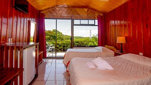 A room with two beds, a small table, a TV, and a view of greenery outside. - Hotel Don Taco (Monteverde)