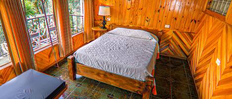 A wooden room with a bed, a table, and a window with curtains.