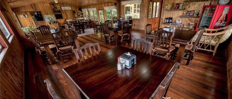 A wooden interior with multiple dining tables and chairs, a kitchen area, and a Coca-Cola refrigerator.