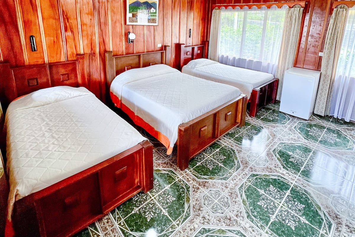 Una habitación con tres camas de madera, un refrigerador blanco pequeño y un cuadro en la pared.